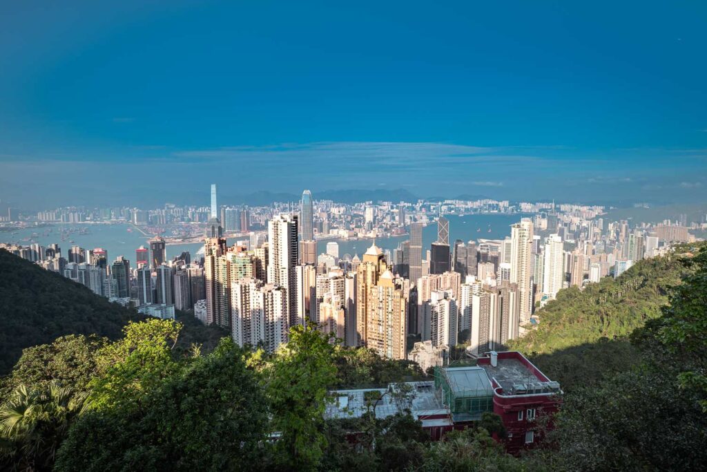 Blick auf die Skyline von Hongkong mit modernen Wolkenkratzern und grünen Bergen im Hintergrund für die Reiseplanung.