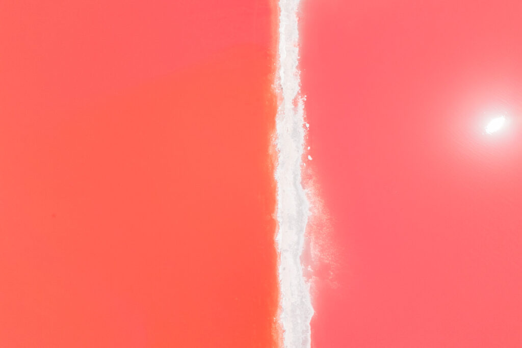 Spektakuläre Drohnenaufnahme der Hutt Lagoon in Westaustralien: Das leuchtend pinke Wasser des Pink Lake wird durch eine strahlend weiße Salzbank in der Mitte geteilt.