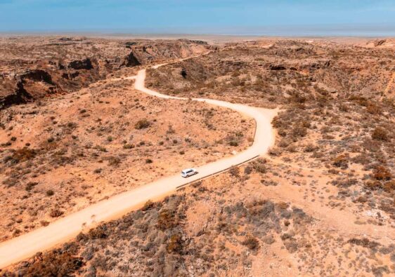 Drohnenaufnahme vom Charles Knife Canyon bei Exmouth in Westaustralien mit einer kurvigen Straße durch die rote Outback-Landschaft und einem weißen Auto.