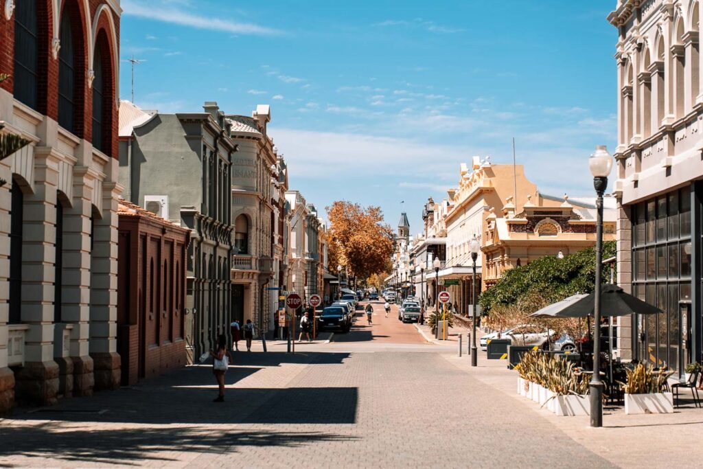 Blick in eine sonnige, historische Straße in Fremantle (Freo), Westaustralien, gesäumt von gut erhaltenen viktorianischen Kolonialbauten unter blauem Himmel.