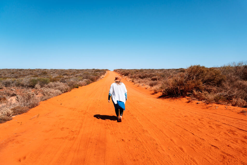 Dani von Auszeit Abenteuer läuft eine einsame rote Sandpiste im Outback von Westaustralien (Francois Peron Nationalpark) entlang unter strahlend blauem Himmel.