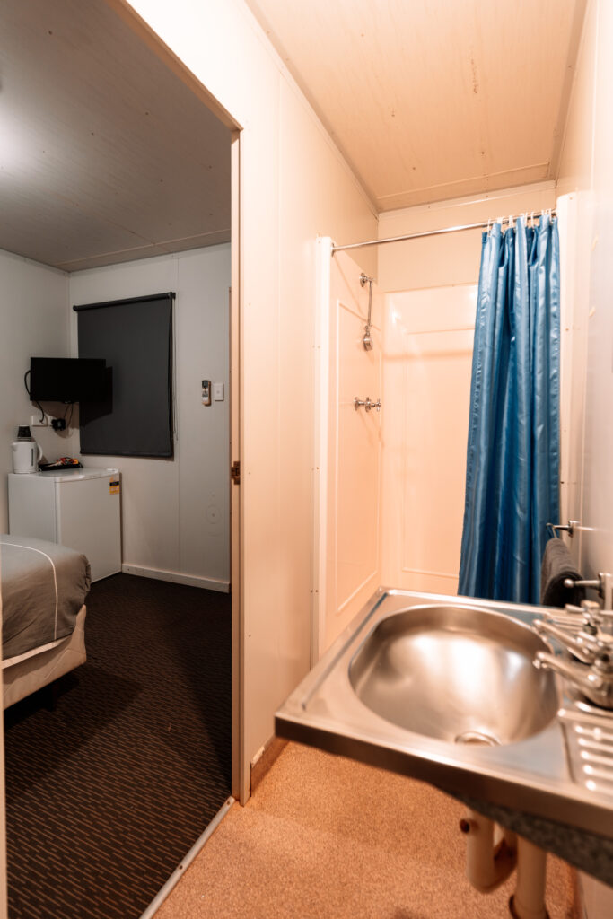 Blick aus dem Badezimmer mit Dusche und Waschbecken auf das Schlafzimmer im Billabong Roadhouse Westaustralien, Auszeit Abenteuer Roadtrip
