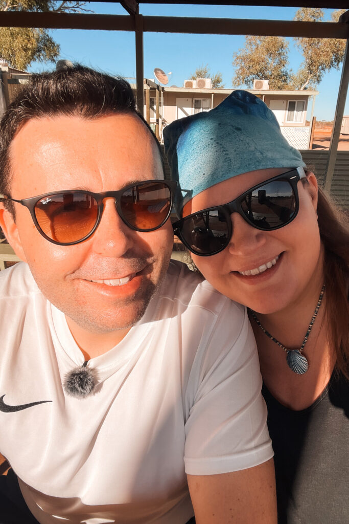 Mario und Dani von Auszeit Abenteuer lächeln in die Kamera. Sie tragen beide eine Sonnenbrille. Billabong Roadhouse, Westaustralien Roadtrip