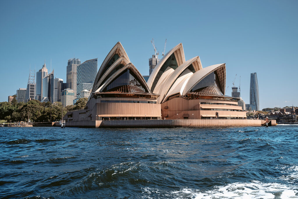 Die wunderschöne Sydney Oper bei blauem Himmel, im Vordergrund das blaue Meer
