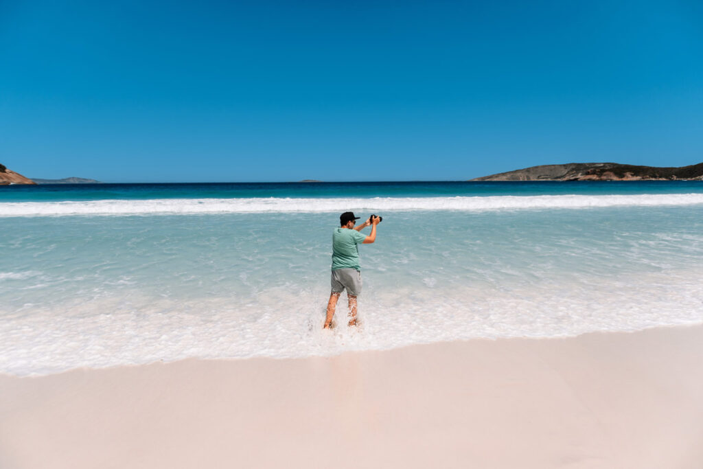 Mario steht knietief im türkisfarbenen Wasser der Hellfire Bay und fotografiert die Landschaft. Die Aufnahme zeigt die beeindruckende Klarheit und Farbe des Ozeans an diesem Strand.