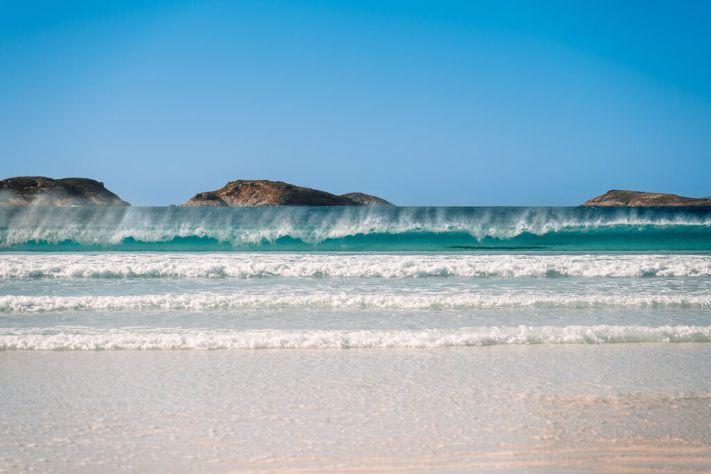 Eine perfekt geformte Welle bricht sich im kristallklaren Wasser der Lucky Bay. Die Aufnahme zeigt die unglaubliche Transparenz und die türkise Farbe des Ozeans.