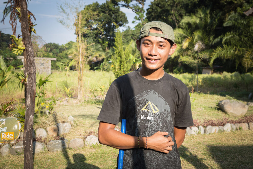 Junger Einheimischer in Bukit Lawang mit Sonnenhut posiert gerne für Reisefotos vor grüner Dschungelkulisse