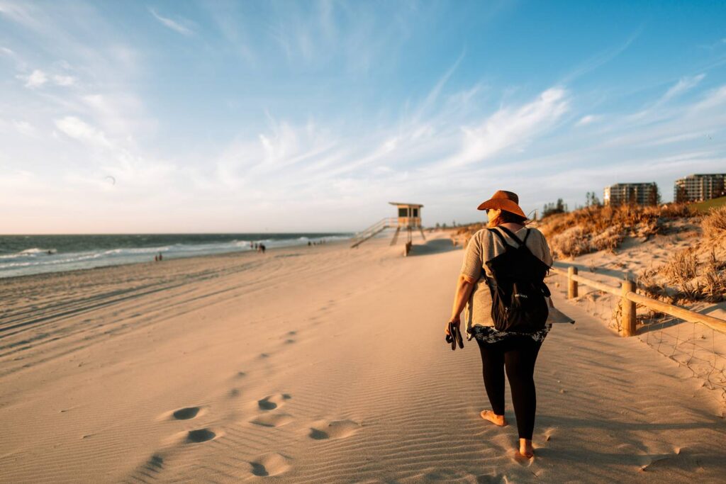 Daniela läuft barfuß im Sand bei einem Strandspaziergang am Scarborough Beach in Perth bei Sonnenuntergang.