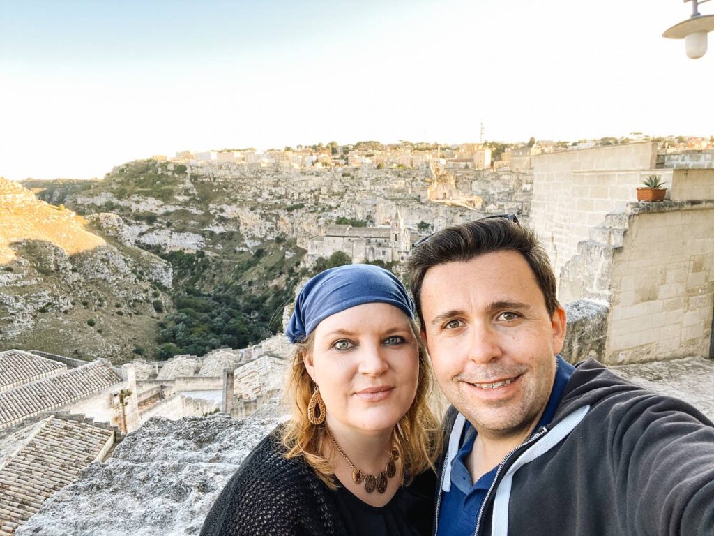 Authentisches Selfie von uns, dem Reisepaar hinter Auszeit Abenteuer, mit der atemberaubenden Kulisse der Sassi di Matera im Hintergrund.