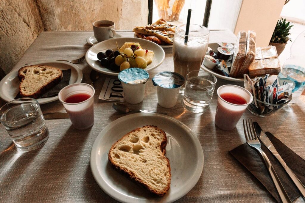 Italienisches Frühstück in Matera mit zwei Tassen Cappuccino, Herz-Latte-Art und lokalen Gebäck-Spezialitäten auf einem Holztisch.