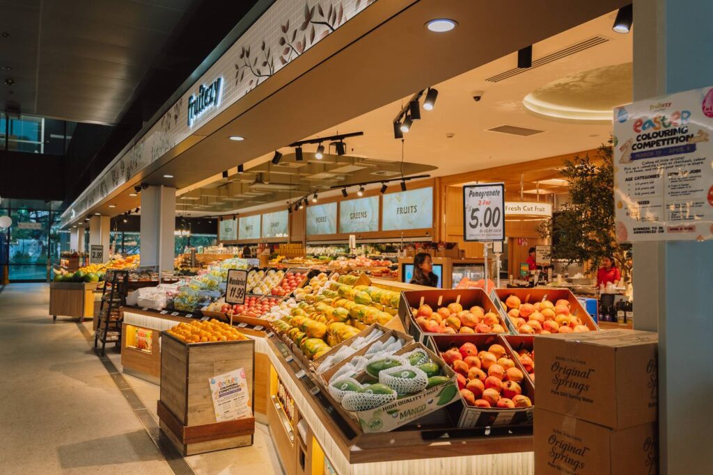 Der moderne Fruitezy-Stand im New Sydney Fish Market präsentiert farbenfrohe Auslagen mit frischen Granatäpfeln, Mangos und Zitrusfrüchten in einer hell erleuchteten Markthalle.