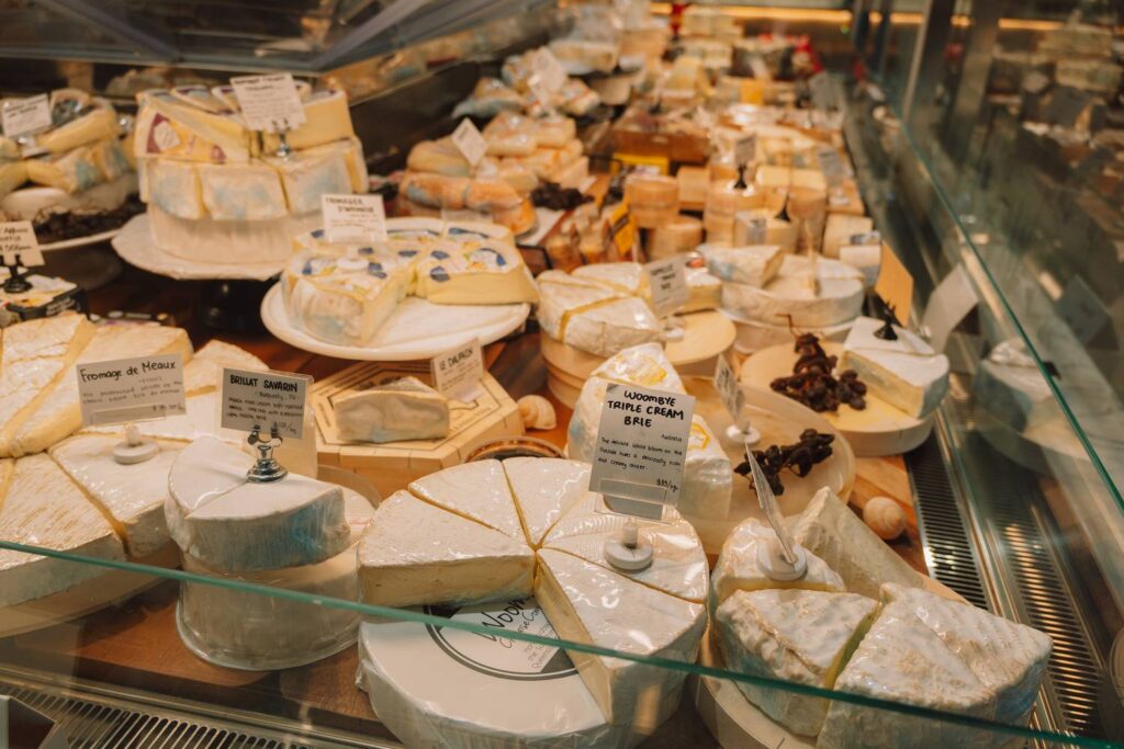 Eine reichhaltige Auswahl an verschiedenen Gourmet-Weichkäsesorten wie Brie und Camembert in einer hell erleuchteten Verkaufstheke auf dem New Sydney Fish Market.