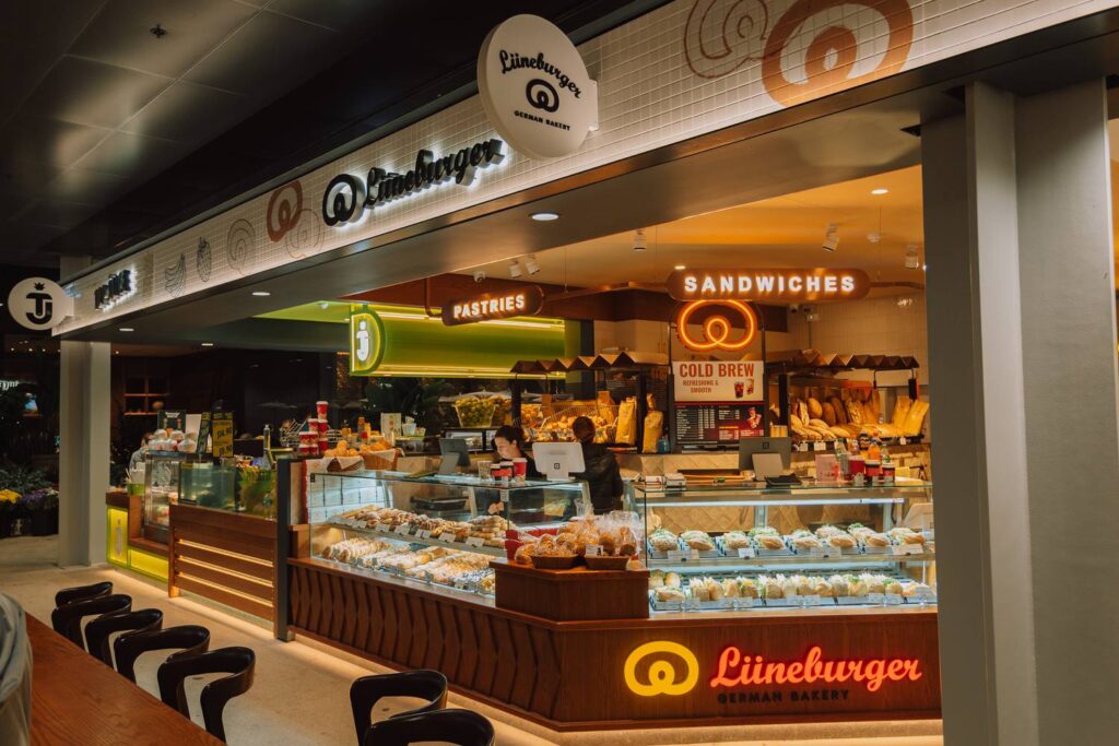 Die modern beleuchtete Lüneburger German Bakery im New Sydney Fish Market präsentiert in warmem Licht eine große Auswahl an frischen Sandwiches und Gebäck in gläsernen Vitrinen.
