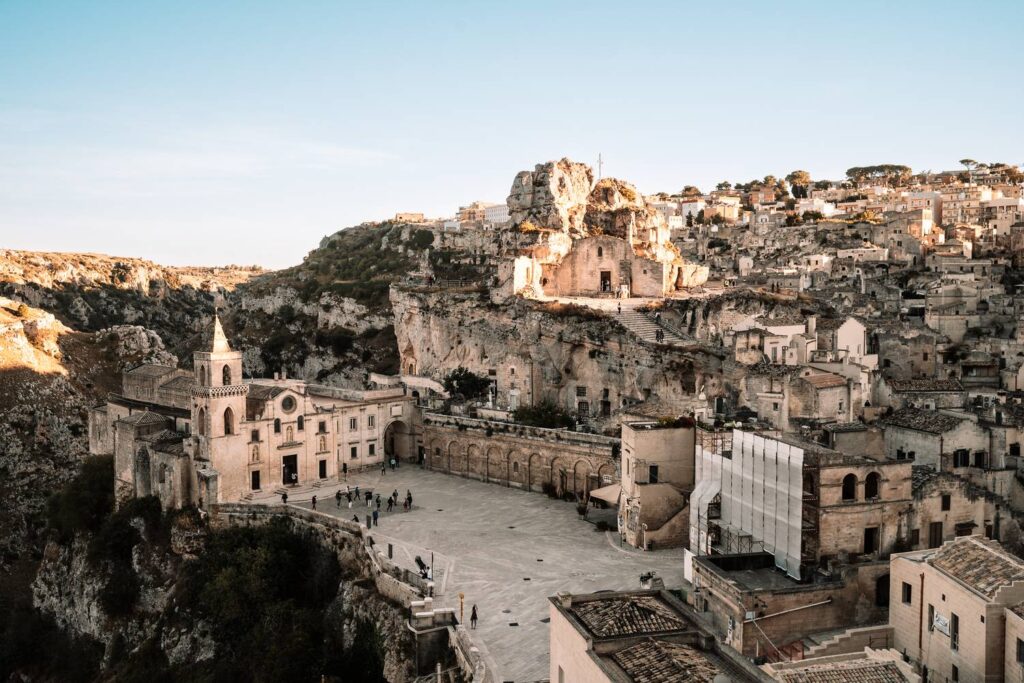 Ein Panoramablick auf die historische Altstadt Sassi von Matera mit der Kirche San Pietro Caveoso und der markanten Felsenkirche Santa Maria de Idris im warmen Abendlicht.