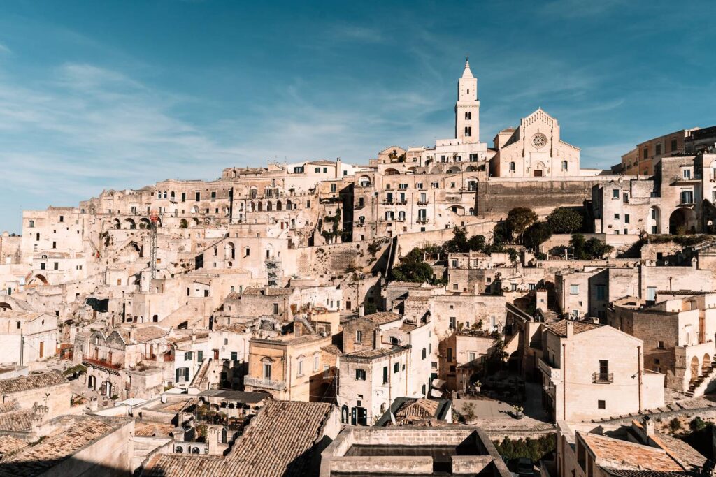 Atemberaubender Blick aus unserem Hotelfenster auf das weiße Steinmeer der Sassi di Matera und den Turm der Kathedrale bei strahlend blauem Himmel.
