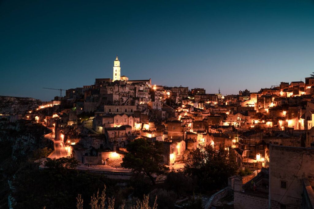 Panoramaaufnahme von Matera bei Nacht: Die beleuchtete Felsenstadt wirkt wie ein goldenes Lichtermeer in der Dunkelheit.