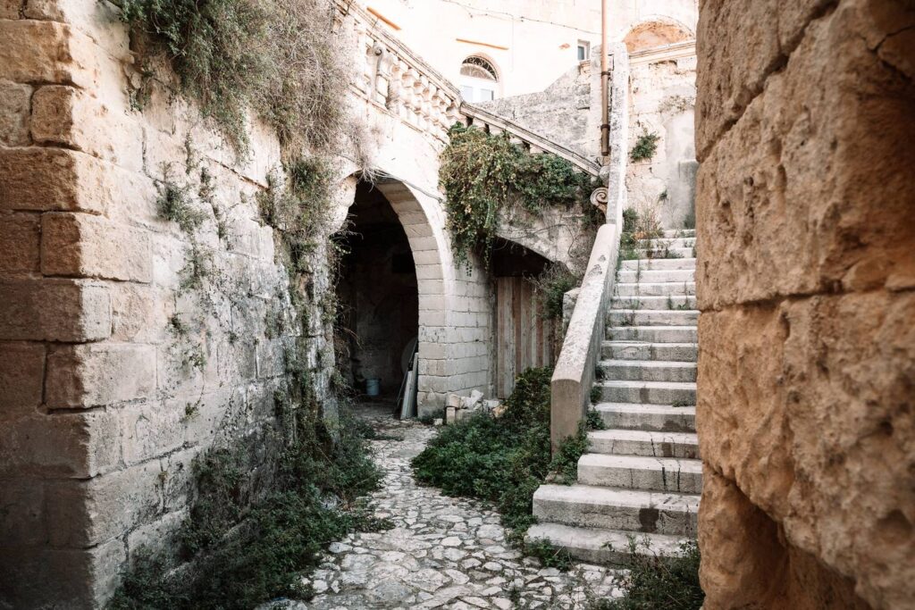 Eine steile, historische Steintreppe in Matera führt durch einen massiven Steinbogen hinauf in die verwinkelten Gassen der Sassi.