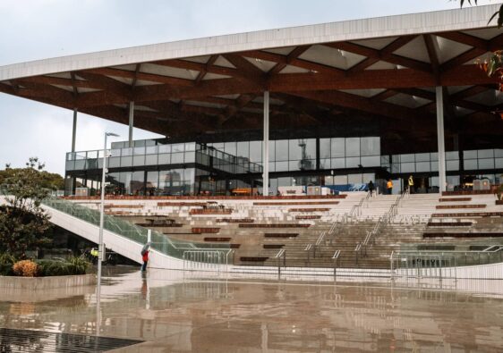 Die moderne Architektur des New Sydney Fish Market mit seinem markanten hölzernen Gitterdach und den weitläufigen Treppenaufgängen spiegelt sich auf dem nassen Vorplatz an einem regnerischen Tag.