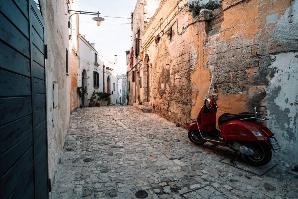 Malerische Gasse in Matera mit typischem Kopfsteinpflaster und einer geparkten roten Vespa.