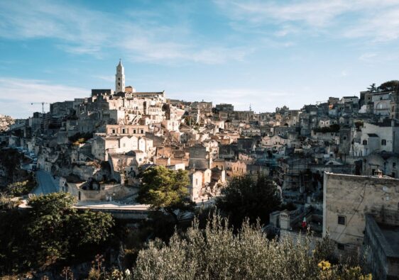 Ein weites Panorama der historischen Altstadt Sassi di Matera in Italien mit ihren dicht gestaffelten, sandfarbenen Steinhäusern und der markanten Kathedrale unter einem klaren blauen Himmel.