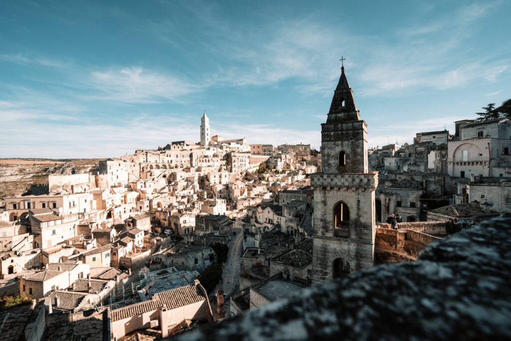 Panoramablick vom Belvedere Luigi Guerricchio über den Stadtteil Sasso Barisano mit dem markanten Turm der Kathedrale von Matera unter blauem Himmel.