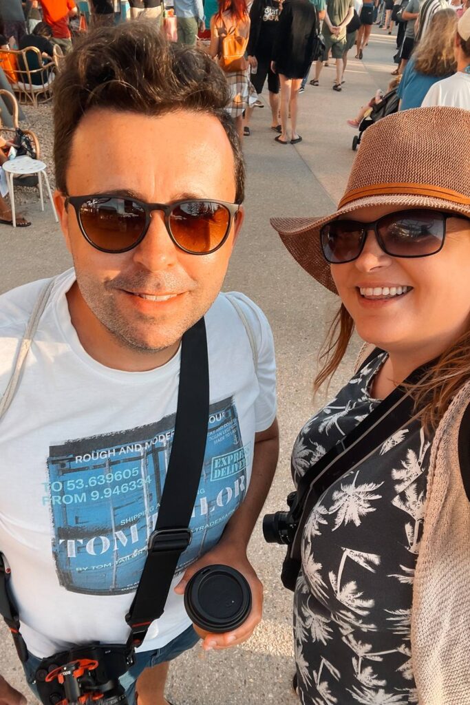 Daniela und Mario von Auszeit Abenteuer mit Sonnenbrillen und Strohhut machen ein Selfie im warmen Abendlicht auf den belebten Sunset Markets in Scarborough bei Perth.