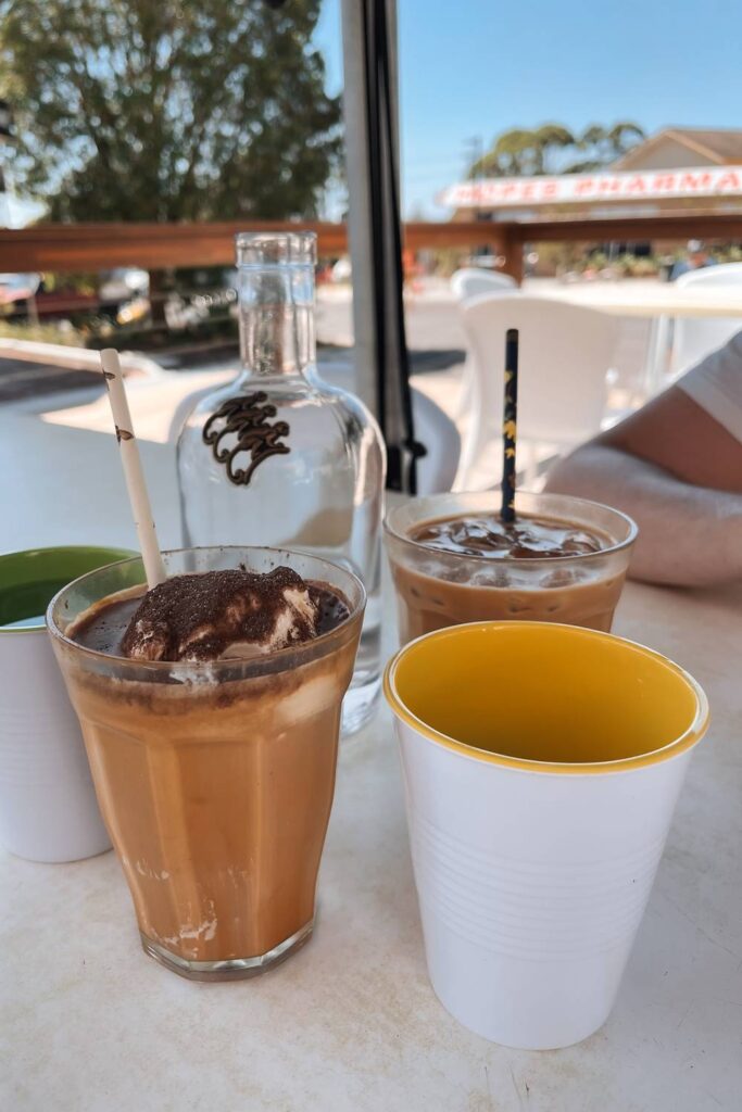 Zwei erfrischende Eiskaffees, einer davon mit Vanilleeis und Kakaopulver garniert, stehen an einem sonnigen Tag auf einem Tisch im gemütlichen Außenbereich eines Cafés in Jervis Bay.