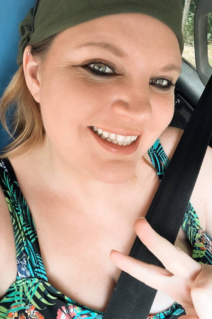 Dani von Auszeit Abenteuer sitzt angeschnallt und gut gelaunt im Auto während eines Roadtrips durch Australien und zeigt ein Peace-Zeichen in die Kamera.