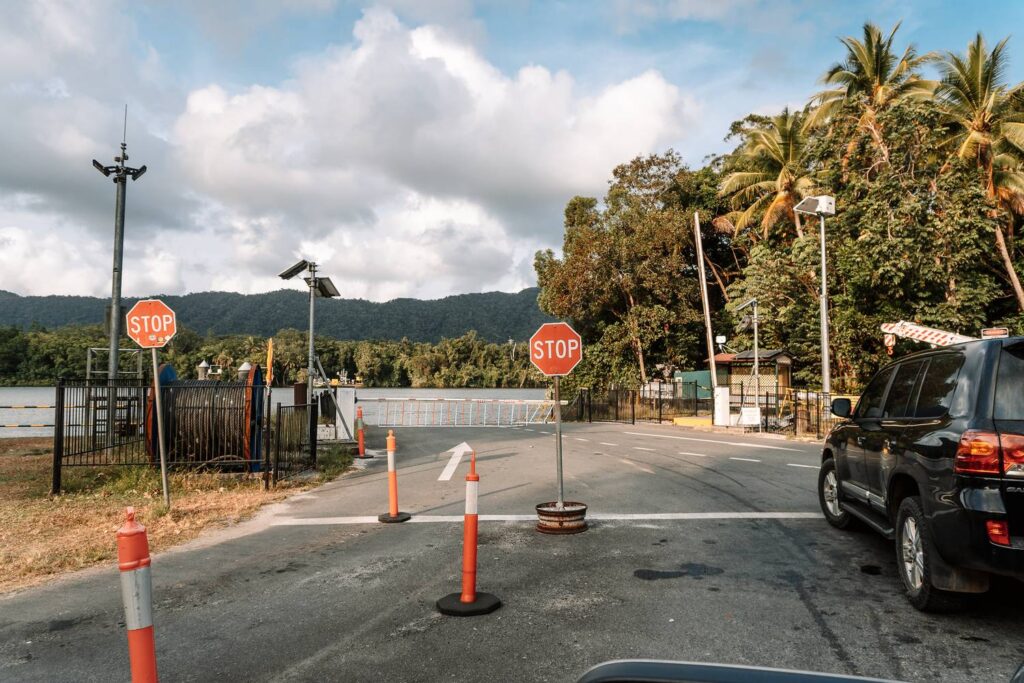 Zufahrt zur Daintree Ferry mit Stoppschildern, Schranke und wartenden Autos vor der Kulisse des dichten Regenwaldes am Daintree River.