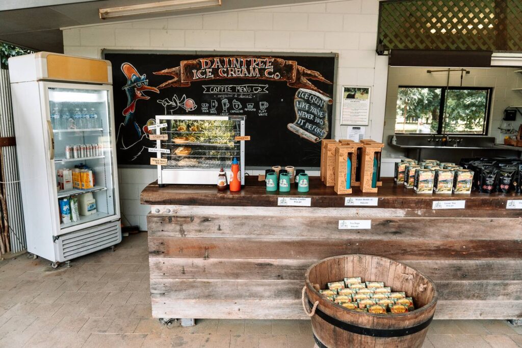 Rustikale Holztheke der Daintree Ice Cream Company mit handbeschrifteter Kreidetafel, Kasuar-Zeichnung, lokalen Souvenirs und Daintree-Tee in einem Holzfass.