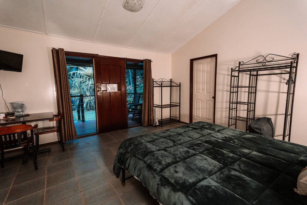 Gemütliches Zimmer der Heritage Lodge im Daintree-Regenwald mit großem Doppelbett und Ausblick durch die Balkontür in die dichte tropische Natur.